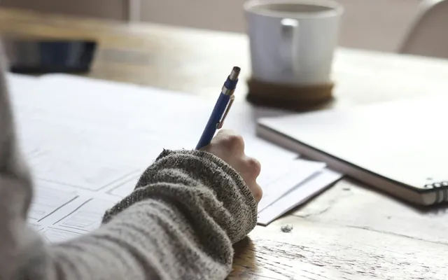 Hand writing notes next to a cup of coffee